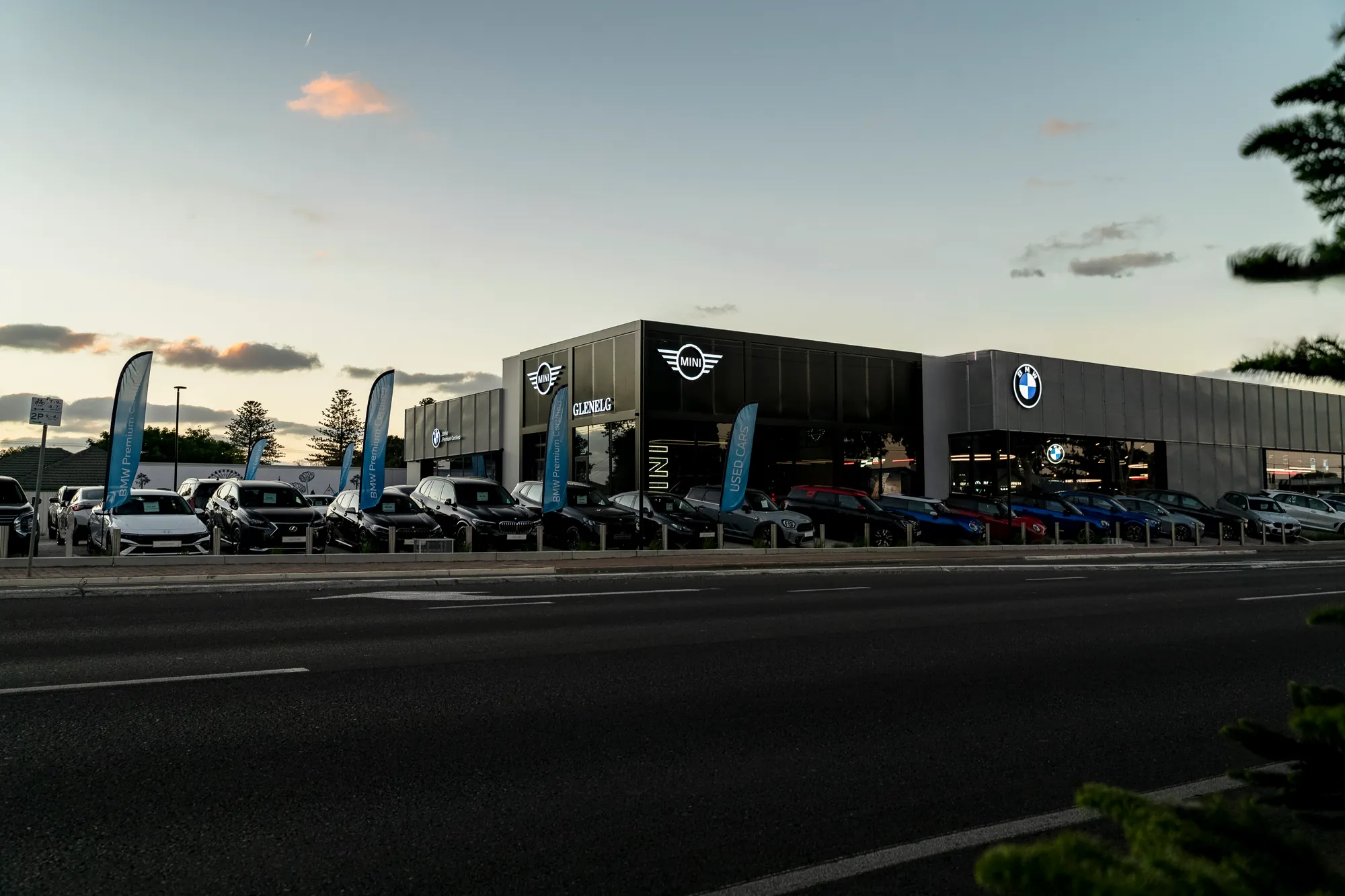 The Glenelg BMW and MINI dealership at dusk, flags along the forecourt