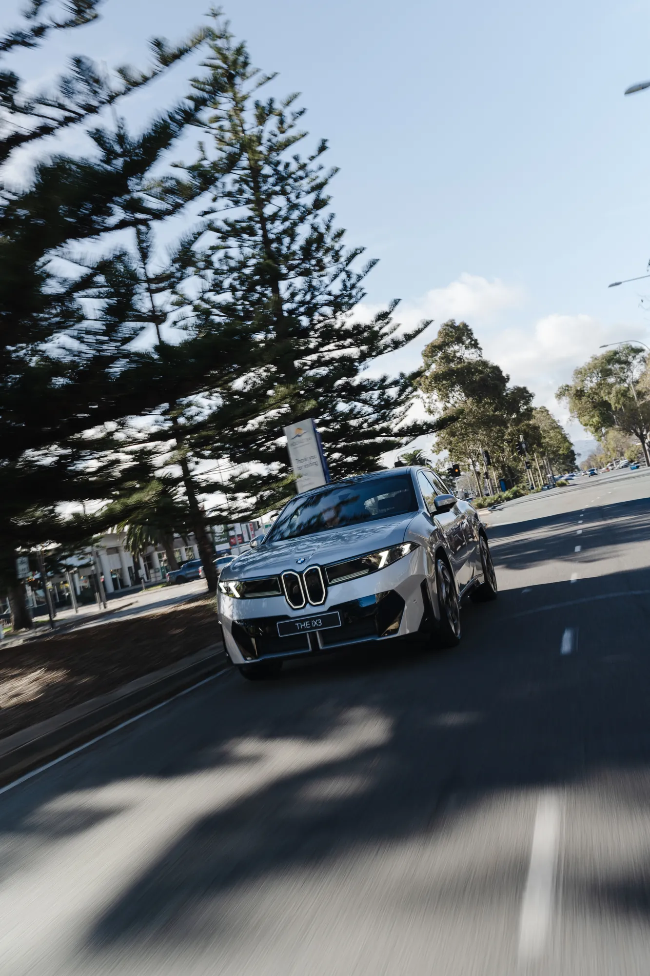A silver BMW sedan moving along a tree-lined Glenelg street