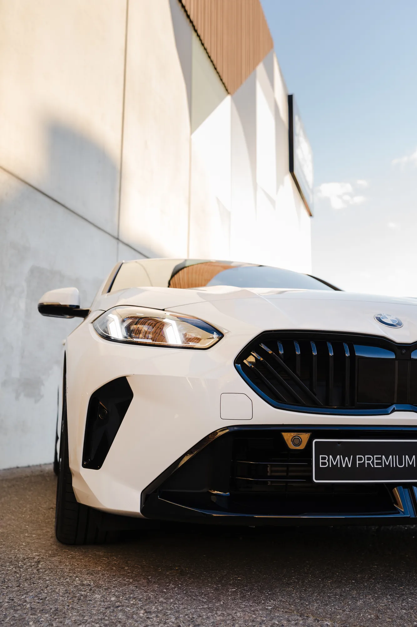 The front quarter of a white BMW against a sunlit wall