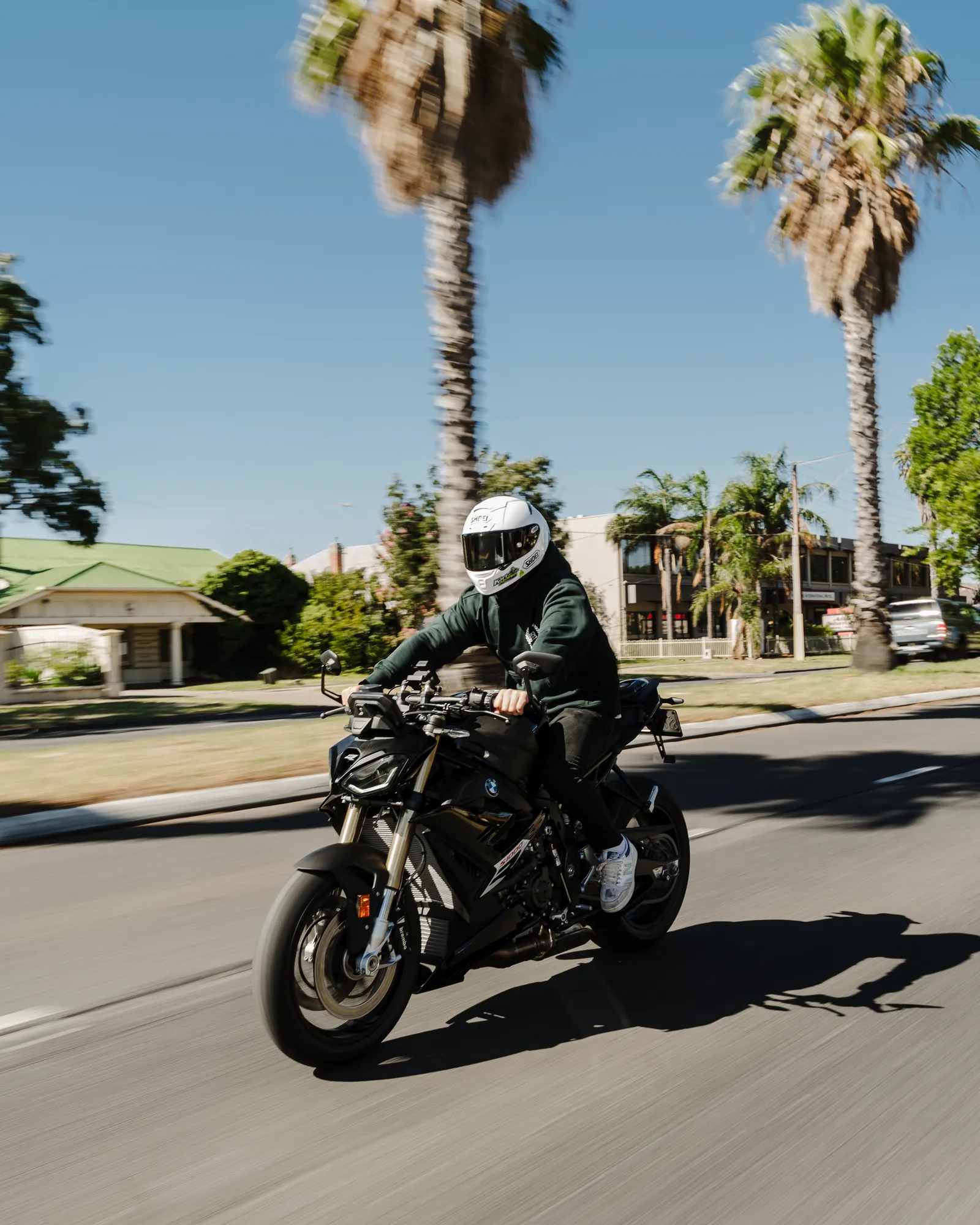 A rider on a BMW motorcycle on a palm-lined Glenelg street