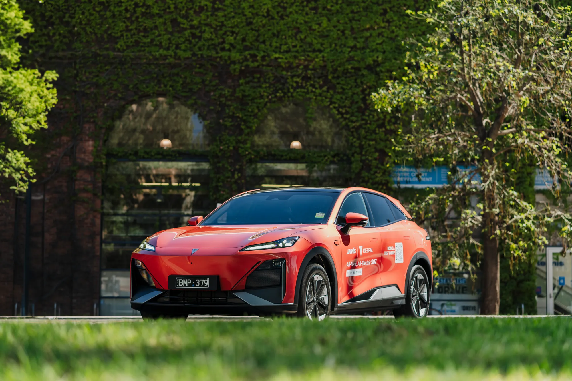 A red Deepal EV parked in front of an ivy-covered brick facade