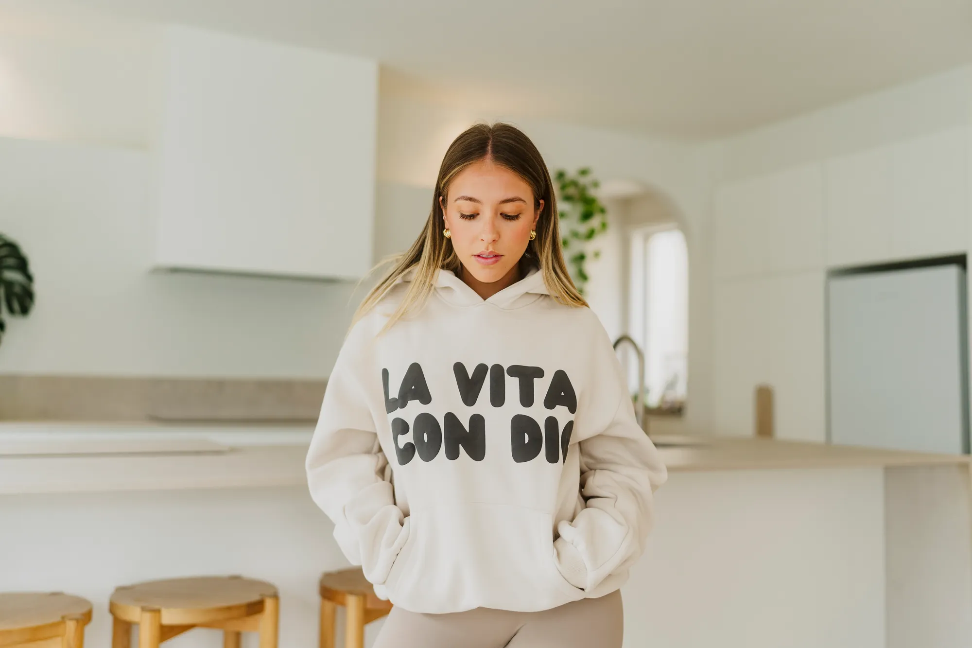 La Vita Con Dio cream hoodie worn in a bright kitchen